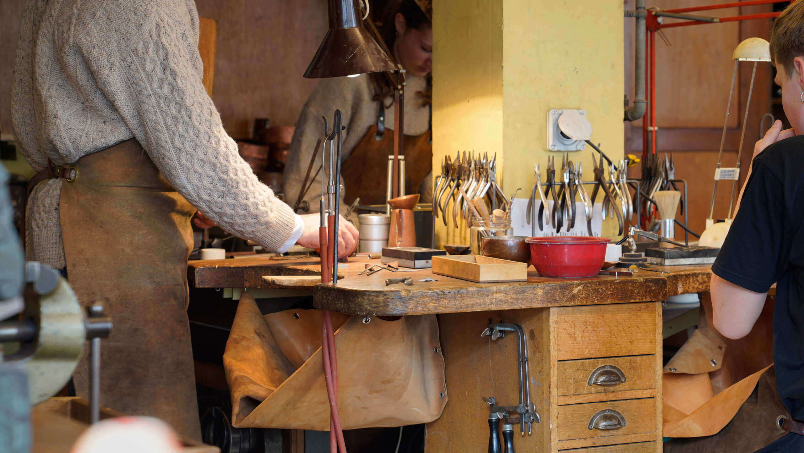Schmuckherstellung in der Metallwerkstatt der Rudolf Steiner Schule Basel: Ein Lehrer und zwei Schüler arbeiten an ihren Schmuckstücken in einer gemütlich anmutenden Werkstatt-Atmosphäre